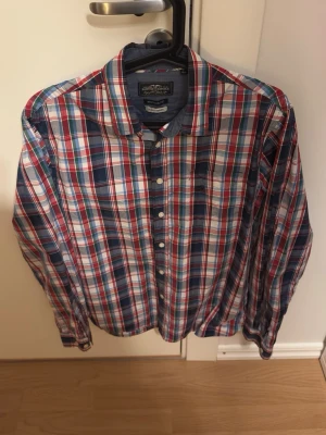 Rutig skjorta Hampton Republic M - Säljer en klassisk rutig skjorta från Hampton Republic i regular fit. Skjortan har långa ärmar, knappar framtill och en bröstficka. Färgerna är röd, blå, grön och vit, och materialet är mjuk bomull. Perfekt till jeans eller chinos för en avslappnad look.