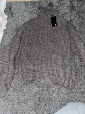 Brun stickad polotröja Minny XS - Säljer en brun stickad polotröja från Minny i storlek XS. Tröjan har ribbade detaljer vid hals och ärmslut, långärmad och loose passform. Perfekt för kyliga dagar och enkel att matcha med jeans eller kjol.