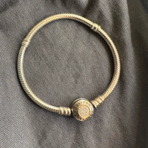 Pandora armband - Pandora Moments Sparkling Crown O Snake Chain-armband i sterlingsilver dekorerat med kubiska zirkoniastenar. Detta är en gammal och unik modell av de kända pandora armbanden. Den är silver, guldrosa och guld färgad. 