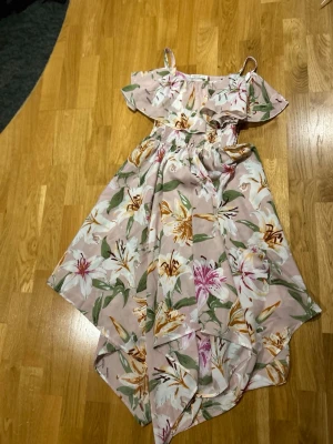 Blommig sommarklänning från Shein Teen 164 - Säljer en ljusrosa blommig klänning från Shein Teen med volang upptill och smala axelband. Klänningen har ett vackert blommönster i vitt, grönt, gult och rosa och är tillverkad i ett lätt syntetmaterial. Perfekt för varma dagar och har en luftig passform.