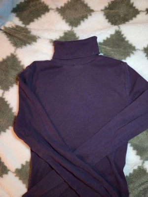 Mörklila polotröja från BikBok - Snygg mörklila polotröja från BikBok i storlek S. Tröjan är ribbad och har lång ärm samt hög polokrage. Materialet är mjuk och stretchig bomull med 5% elastan, vilket gör den bekväm och följsam. Perfekt för lager-på-lager under kyliga dagar.