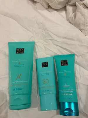 Rituals The Ritual of Karma hudvård - Tre produkter från Rituals The Ritual of Karma-serien: en after sun hydrating lotion (200 ml), en solskyddskräm för ansiktet SPF 30 (50 ml) och en handkräm med hydra-boost complex (70 ml). Alla i snygga turkosa tuber med vita och guldiga detaljer.