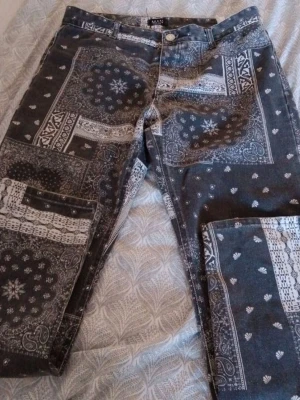 NYA Svarta mönstrade jeans från boohooMAN - Unika svarta jeans från boohooMAN med coolt paisley och bandana-mönster i vitt. Klassisk femficksmodell med knapp och dragkedja fram. Materialet är jeans och passformen är normal. Perfekt för dig som vill sticka ut med din stil. Storlek L