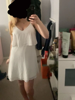 Vit somrig kortklänning med volang - Säljer en superfin vit kortklänning med tunna axelband och v-ringning. Klänningen har en snygg volangdetalj över bysten och är gjord i ett lätt material som passar perfekt till varma dagar. Enkel och stilren design som känns fräsch och modern.