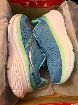 Saucony Guide 17 Breeze/Mint sneakers STORLEK 40 - Saucony Guide 17 sneakers i färgen Breeze/Mint. Skorna har en ventilerande mesh-ovandel i blått med mintgröna detaljer och en tjock, vit platt sula. Klassisk snörning och rund tå. Perfekta för träning och löpning, med bekväm passform och snygg design.