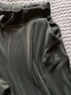 Gröna Juicy Couture mjukisbyxor - Säljer ett par gröna mjukisbyxor från Juicy Couture i mjuk sammet. Byxorna har breda ben, snörning i midjan och fickor. På baksidan står det 'Juicy' i glittriga stenar och framtill finns en liten JC-logga. Perfekta för en chill och trendig look.
