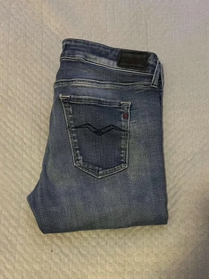 Replay Anbass jeans blå denim - Säljer ett par snygga Replay Anbass jeans i klassisk blå denim med coola detaljer på bakfickan. Jeansen har en slim passform och är tillverkade i mjukt jeansmaterial med lätt tvättad look. Perfekta för dig som gillar stilrena och bekväma jeans.