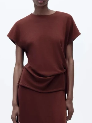 Vinröd topp med knyt från Zara - Säljer en vinröd topp från Zara med rund hals och korta ärmar. Toppen har en snygg knytning i sidan som ger en cool draperad effekt. Materialet är mjukt och känns bekvämt mot huden. Perfekt att styla med jeans eller kjol för en trendig look.