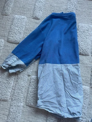 Blå och vit randig topp från COS - Säljer en cool topp från COS i storlek S. Överdel och ärmar är i blått, medan nederdelen och ärmsluten har ett vitt och blått randigt mönster. Materialet är en mix av bomull och syntet, med en normal passform och trekvartsärm. Perfekt för dig som gillar stilrena detaljer. (Jag stryker den innan jag skickar!)