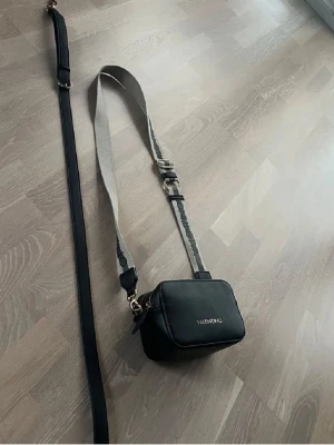 Svart axelväska från Valentino - Snygg axelväska från Valentino med justerbar rem och gulddetaljer. Väskan ett extra fack på baksidan och två inuti, ett i varje. Man ser inte att den använts ett flertal gånger, ser ut att vara i nyskick. supersnygg och perfekt för att bära dina nödvändigheter och annat med stil. Rätt så rymlig. Bra pris med tanke på vad den köptes för