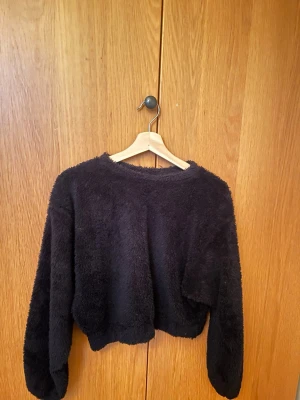 Svart fluffig croppad tröja i teddy-material - Mysig svart croppad tröja med lång ärm och rund hals. Tröjan är gjord i ett fluffigt och mjukt material som ger en skön känsla. Perfekt för kyliga dagar när du vill vara både bekväm och snygg. Har klippt bort lappen, men är köpt från Pull&Bear och passar en S.