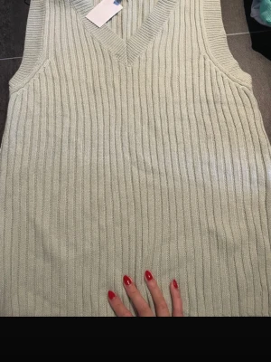 Ljus grön ribbad stickad väst Divided - Säljer en ljus grön stickad väst från Divided i storlek M. Västen har ribbad struktur och v-ringad hals, perfekt att styla över en skjorta eller t-shirt. Materialet är mjukt och skönt, och den har en clean, enkel look.