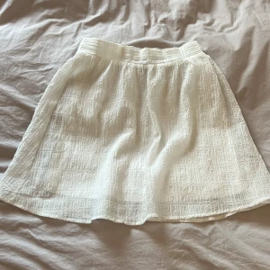 Vit kortkjol från H&M Divided - Säljer en vit kortkjol från H&M Divided i storlek 34. Kjolen har en lätt strukturerad yta och är gjord i polyester med stretchig underkjol. Inte alls genomskinlig och saknar fläckar och slitage.