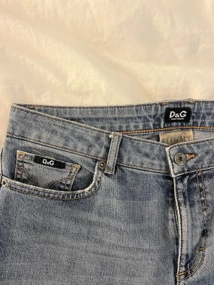 D&G ljusblå jeans - Säljer ett par ljusblå jeans från D&G med klassisk femficksdesign och snygga detaljer som logopatch på bakfickan. Modellen är rak med låg midja och normal passform. Jeansen är tillverkade i bomull.
