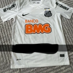 Santos Neymar Jr 11 Nike fotbollströja - Santos FC officiell matchtröja med Neymar Jr och nummer 11 på ryggen. Vit med svarta detaljer, klubbmärke och Nike-logga på bröstet samt sponsortryck i orange. Tillverkad i Dri-FIT-material för bästa komfort på planen. Kortärmad och autentisk modell.