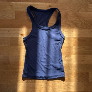 Marinblå ribbad linnetopp - Säljer en marinblå ribbad linnetopp med klassisk racerback och rundad hals. Toppen är ärmlös och har en tight passform som sitter snyggt mot kroppen. Perfekt för dig som gillar enkel och stilren design.