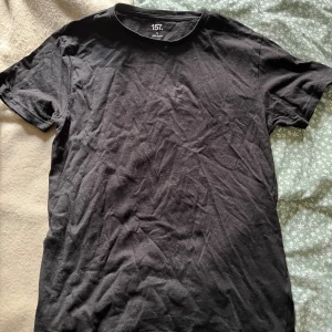 Svart basic t-shirt från 157 - Enkel svart t-shirt från 157 i klassisk modell. Gjord i mjuk bomull med rund hals och korta ärmar. Perfekt till jeans eller shorts för en clean och stilren look.