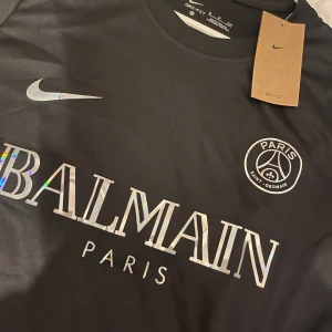 Svart PSG x Balmain fotbollströja Nike - Snygg svart fotbollströja från Nike i samarbete med PSG och Balmain. Tröjan har klassisk rund hals, korta ärmar och är tillverkad i ett lätt och svalt funktionsmaterial. Som kostar 400 kr och är s storlek 