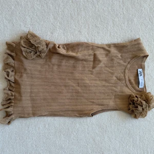 Beige kortklänning med volang från Zara - Supersöt beige kortklänning från Zara med ribbad struktur och volangdetaljer i spets vid axel och nederkant. Ärmlös modell som ger en chill och trendig vibe, perfekt för dig som gillar att sticka ut med detaljer. Passar dig som vill ha något unikt och stilrent.