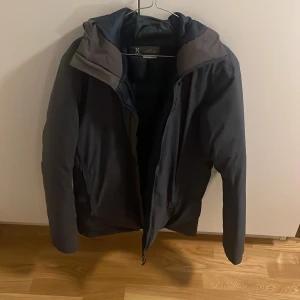 Svart dunjacka från Haglöfs med huva - Säljer en grå dunjacka från Haglöfs i storlek M. Jackan har en snygg, enkel design med huva och dragkedja framtill. Insidan är vadderad i mörkblått och jackan har två fickor med dragkedja. Perfekt för kalla dagar och outdoor. Helt ny jacka sällsynt