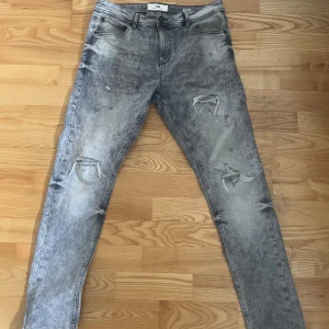 Grå jeans med slitningar - Snygga grå jeans med slitningar för en trendig look. De har en klassisk femficksdesign och knappgylf. Perfekta för en avslappnad stil. Pris kan diskuteras 