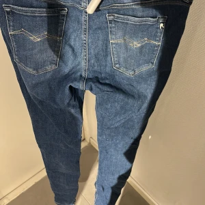 Replay blå jeans med raka ben - Säljer ett par klassiska blå jeans från Replay med raka ben och snygga kontrastsömmar. Jeansen har fem fickor, normal passform och är tillverkade i mjukt denimtyg. Perfekta för dig som gillar en tidlös look med diskreta detaljer.