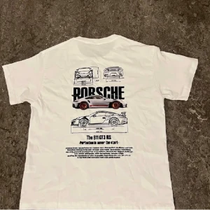 Vit Porsche 911 GT3 RS t-shirt - Vit t-shirt med tryck av Porsche 911 GT3 RS på ryggen. Stora svarta bokstäver, detaljerade bilskisser och färgglad bilgrafik gör den riktigt snygg. Klassisk passform med rund hals och korta ärmar. Perfekt för dig som älskar bilar och motorsport.