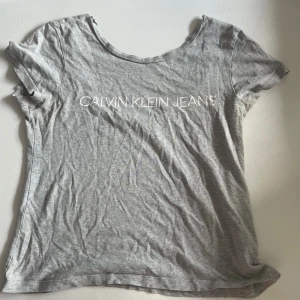 Grå Calvin Klein Jeans t-shirt - Grå t-shirt från Calvin Klein Jeans med vit logga framtill. Klassisk rund halsringning och korta ärmar. Tunt och mjukt material som känns skönt mot huden, perfekt för en avslappnad look.