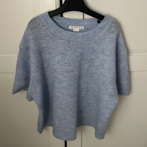 Ljusblå stickad tröja från Gina Tricot - Supermysig ljusblå stickad tröja från Gina Tricot med korta ärmar och bred ribbad rund halsringning. Tröjan har loose passform och är perfekt för lager-på-lager. 