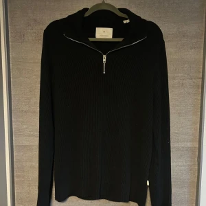 Svart stickad half zip från Jack & Jones - Svart stickad tröja från Jack & Jones med ribbad struktur och half zip-dragkedja vid halsen. Långärmad och med en clean, stilren look som funkar till jeans eller chinos. Perfekt för dig som gillar enkel och snygg stil.