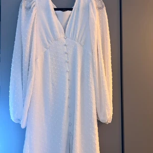 Vit elegant klänning med prickig struktur - Superfin vit klänning från Veromoda med transparenta långärmar och prickig struktur. Det är v-ringning och knappar framtill. Det är storlek S