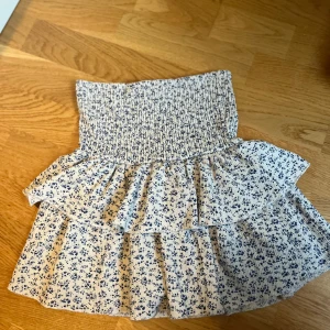 Blommig volangkjol från Zara med shorts i - Supersöt kort volangkjol från Zara i vitt med små blå blommor. Kjolen har smock i midjan och dubbla volanger som ger en luftig och somrig känsla. Perfekt för dig som gillar romantisk och trendig stil. Med shorts i