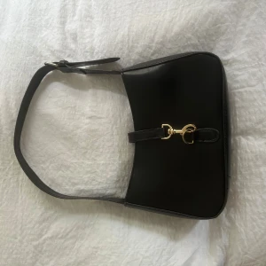 Svart axelväska med gulddetaljer - Får plats med telefon, korthållare, läppenna, läppglans o 30 ml parfymflaska.