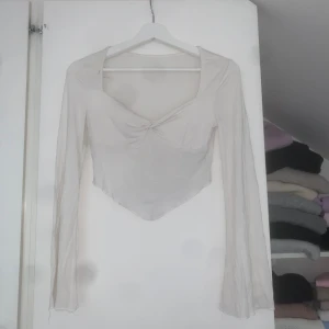 Vit croppad topp från SHEIN  - Säljer en vit långärmad croppad topp från SHEIN i storlek XS. Toppen har v-ringning med twistad detalj framtill och asymmetrisk nederkant. Tunt och lätt material.