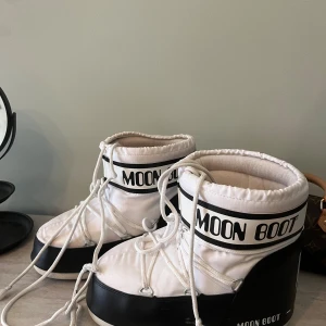 Vita och svarta Moon Boots - Säljer ett par klassiska Moon Boots i vitt och svart med tydlig logga runt skaftet. Skorna har snörning framtill och är tillverkade i syntetmaterial med vadderad insida för extra värme. Perfekta för vintern och riktigt snygga till vinterlooken.
