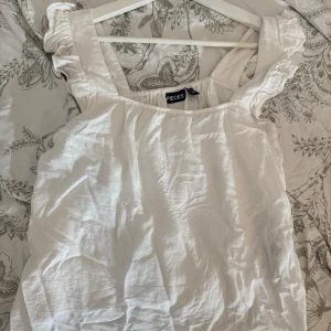 Vit linnetopp från Pieces XS - Säljer en söt vit linnetopp från Pieces i storlek XS. Toppen har breda axelband med volangdetaljer och är tillverkad i ett luftigt linnematerial, perfekt för varma dagar. Enkel och stilren design som är lätt att matcha med olika outfits.