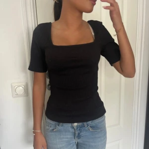 Svart ribbad topp med fyrkantig ringning - Säljer en svart ribbad topp med korta ärmar och snygg fyrkantig ringning. 