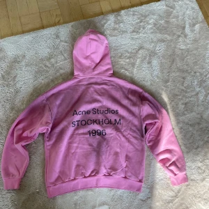 Rosa hoodie från Acne Studios - Säljer en oversized rosa hoodie från Acne Studios med tryck på ryggen: 'Acne Studios STOCKHOLM 1996'. Tröjan har huva, ribbade muddar och är tillverkad i mjuk bomull. Perfekt för dig som gillar streetwear och vill sticka ut med färg. Ny pris 5300