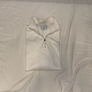 Vit half zip tröja från Bläck - Säljer en stilren vit långärmad tröja från Bläck i storlek S. Tröjan har en klassisk half zip-dragkedja och ribbade muddar vid ärmslut och nederkant. Perfekt för lager-på-lager och enkel att matcha med det mesta. Kostar 700kr helt ny från MQ