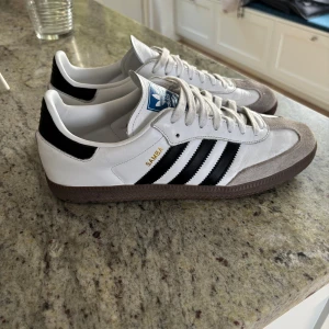 Adidas Samba vita och svarta sneakers - Klassiska Adidas Samba sneakers i vitt skinn med svarta detaljer och bruna gummisulor. Använda typ 3 gånger.