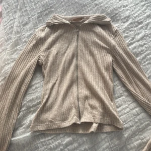 Beige ribbad kofta från 157 XS - Säljer en beige ribbad kofta från 157 i storlek XS. Koftan har dragkedja framtill, långärmad design och mjukt stickat material. Perfekt för lager-på-lager och chill dagar. Snygg krage och diskret färg som passar till allt.