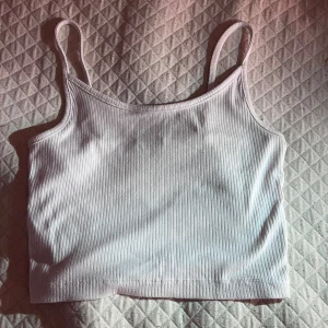 Vit ribbad linnetopp med smala band - Säljer en enkel och stilren vit ribbad linnetopp med smala axelband. Toppen är croppad och har en tight passform som sitter snyggt på kroppen. Perfekt för varma dagar eller att styla lager på lager. Materialet känns mjukt och stretchigt!🫶🏼