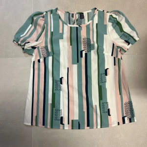 Randig blus från Shein i pastell - Säljer en blus från Shein med pastellfärgade ränder i grönt, rosa, vitt och blått. Blusen har korta puffärmar och rund halsringning. Mönstret är grafiskt med inslag av små svarta prickar. Perfekt för dig som gillar färg och mönster!