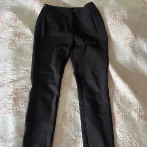 Svarta kostymbyxor från Zara  - Svarta kostymbyxor från Zara med raka ben och diskreta fickor fram. Byxorna har en elastisk midja med vit randig detalj bak och är tillverkade i ett mjukt, bekvämt material. Perfekta för en clean och stilren look.