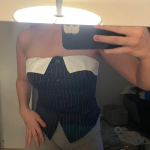 Randig tubtopp med skjortkrage - Snygg tubtopp i mörkblått med vita ränder och en vit skjortkrage upptill. Toppen har knappar framtill och en unik skjortliknande design som ger en cool och edgy vibe. Perfekt för dig som vill sticka ut med en annorlunda och trendig look.