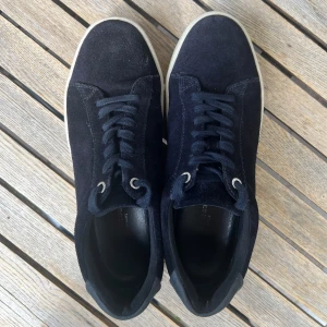 Svarta mockasneakers från Vagabond - Snygga svarta sneakers från Vagabond i mocka med klassisk rund tå och vit platt sula. Skorna har snörning och diskret logga på sulan. Perfekta för dig som gillar stilrena och tidlösa sneakers med en lite lyxigare känsla. Modell Zoe unisex. Färg: indigo. Nypris 1100kr. Skicket är bra och jag har haft dessa sneakers sedan julafton 2021