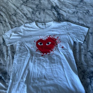 CDG Tshirt - En CDG tshirt med ett stort rött hjärta och färgstänk. Sitter ”regular”