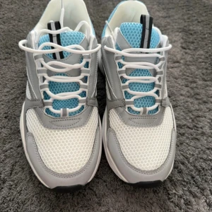 Dior b22 sneakers i vitt, grått och blått - Chunky Dior sneakers med vit mesh, gråa och blå detaljer samt svarta inslag. Skorna har snörning, rund tå och platt sula. Ovandelen är i mesh och syntet med coola bikakemönstrade partier och märkning på sulan. Perfekta för dig som gillar statement sneakers. De kommer utan låsan då den är förstörd, men resten kommer med på köpet😊 skriv innan du köper tack.