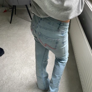 Nelly jeans - Ett par snygga Nelly jeans med bootcut passform och låg midja. Jeansen har slitna hål vid knäna och coola rosa sömmar på bakfickorna. Tillverkade i klassiskt denimtyg med femficksmodell och dragkedjegylf. Midjemått 34cm rakt över och innrebens längd är 73cm. Använda 1 gång. Diskuterbart pris.🥰
