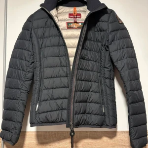 Svart lättviktsdunjacka Parajumpers XS - Snygg svart dunjacka från Parajumpers i storlek XS. Jackan är quiltad och superlätt, med dragkedja framtill och två sidofickor med dragkedja. Insidan är ljusgrå och har en praktisk innerficka märkt 'Security Pocket'. Perfekt för höstliga dagar.